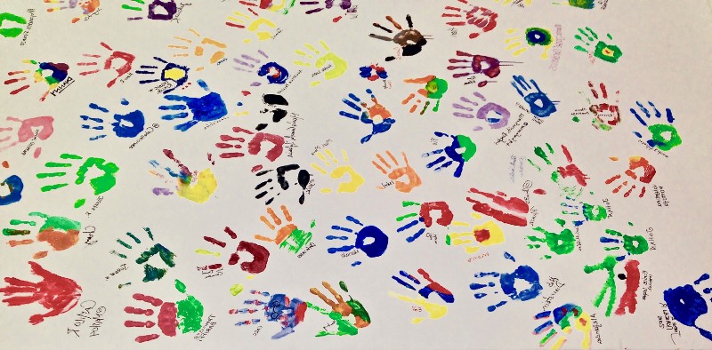 Many multicoloured handprints in paint on a large sheet of paper
