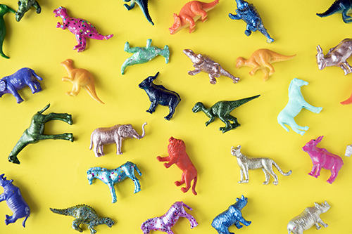 Many colourful plastic animal and dinosaur toys on a yellow background